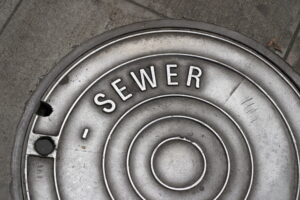 A sewer manhole cover in the sidewalk that is well worn and shiny